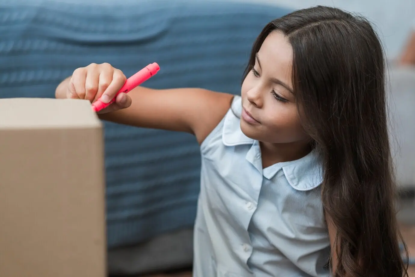 Девочка рисует фломастером на картонной коробке.